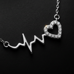 A 925 sterling silver rhodium polished necklace by CHAKORE featuring an EKG heartbeat line pendant that transitions into a heart-shaped halo encrusted with small clear stones, shown on a dark textured background.