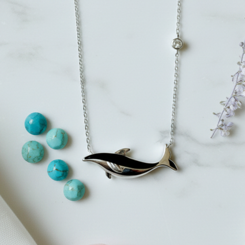925 Sterling Silver Black Enamel Whale Pendant Necklace with Bezel Accent – Flat Lay on White Marble with Dried Flowers.