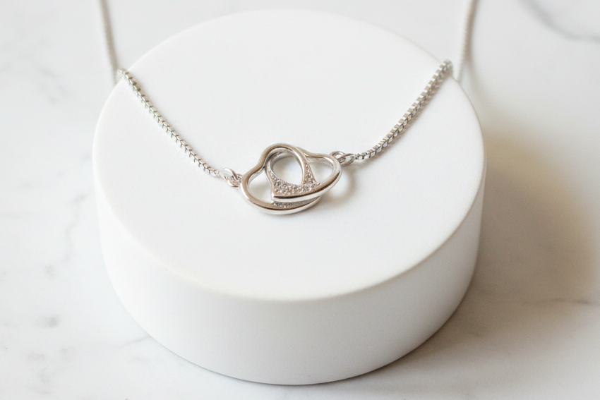 925 sterling silver free-moving interlocked open hearts necklace displayed on elevated white marble platform – minimalist luxury flat lay jewelry photography
