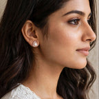 A close-up side profile of a woman wearing a small teardrop-shaped pearl stud earring with a gold-toned setting.