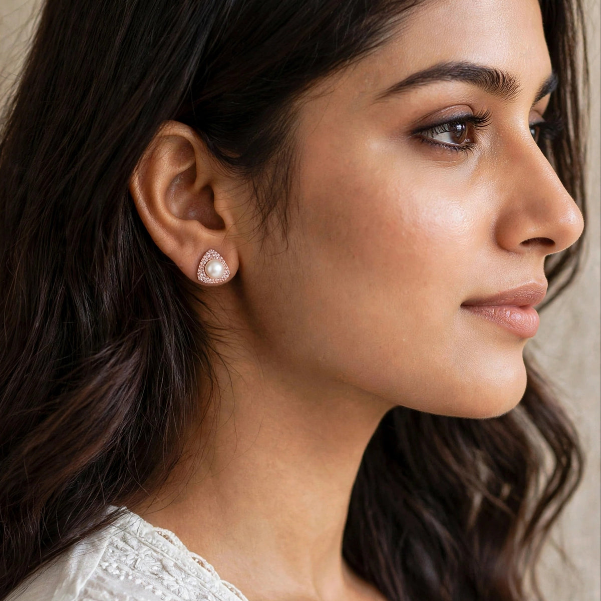 A close-up side profile of a woman wearing a small teardrop-shaped pearl stud earring with a gold-toned setting.
