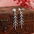 Silver tree-shaped earrings on a wooden box with floral patterns