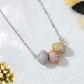 A 925 sterling silver necklace featuring three horizontal oval pavé-set beads in silver, rose gold, and yellow gold finishes. The tri-color pendant and attached silver box chain rest flat on a white textured background, accented by dark green leaves and small dried yellow and white flowers. Modern minimalist silver jewelry, mixed metal styling, everyday wear.