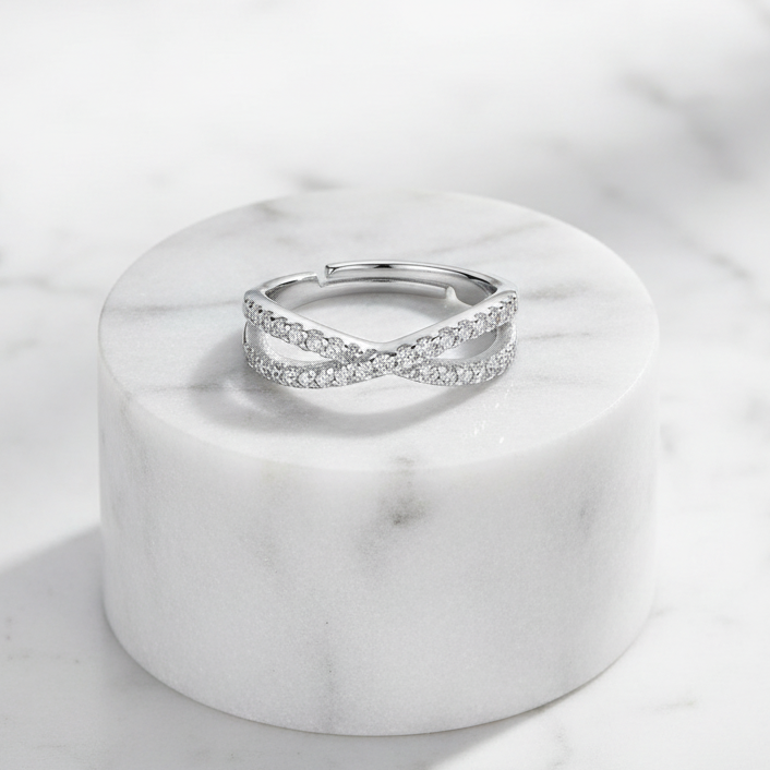Crossover Infinity 925 Sterling Silver Ring by CHAKORE with Pavé Cubic Zirconia – Adjustable Band on Marble pedestal flat lay