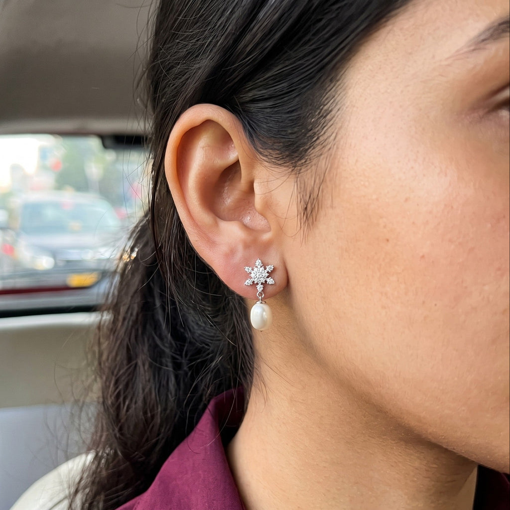 A close-up of a woman's ear wearing a 925 silver flower-shaped stud earring by Chakore with a white pearl drop, photographed inside a car.
