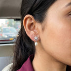A close-up of a woman's ear wearing a 925 silver flower-shaped stud earring by Chakore with a white pearl drop, photographed inside a car.