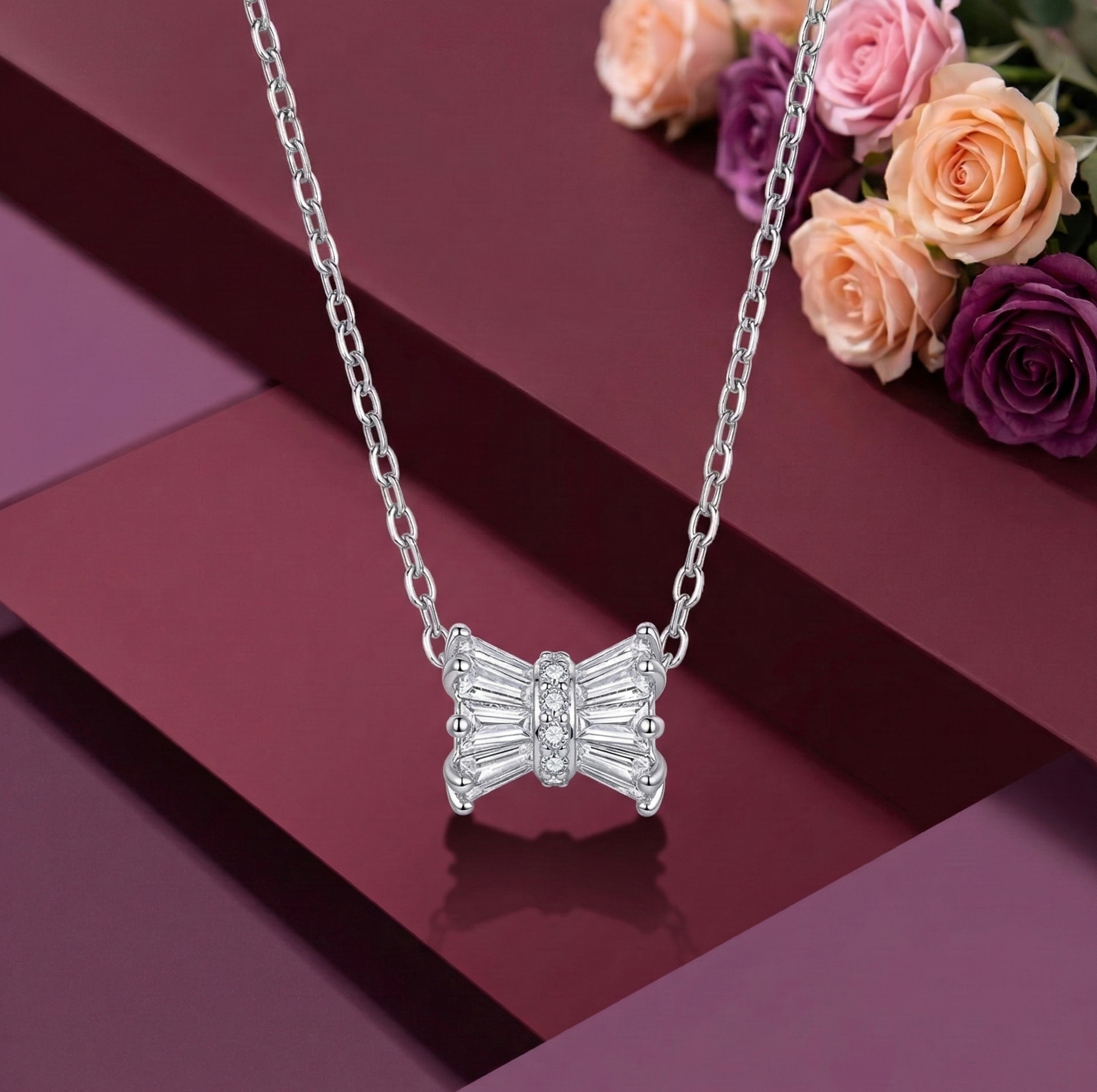A modern 925 sterling silver necklace featuring a stylized Damru pendant crafted from sparkling baguette-cut cubic zirconia stones with a pavé center. The elegant spiritual Hindu jewelry is suspended over a rich burgundy geometric background, accented with soft pink and deep purple roses. Modern Indian D2C silver jewelry, Shiva Damru necklace, high-polish rhodium finish.