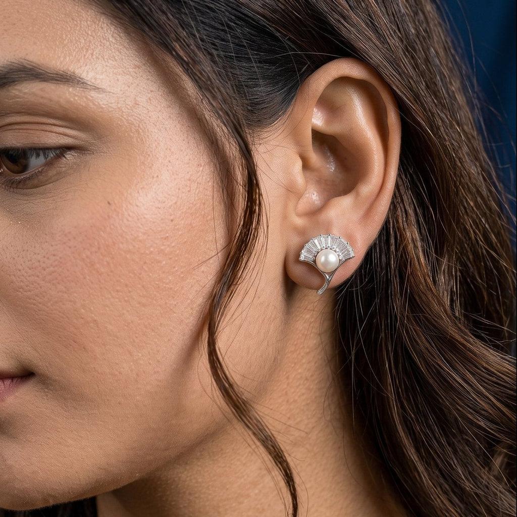A close-up side profile of a woman wearing a small 925 silver stud earring with a clear faceted real freshwater pearl on a dark blue background.