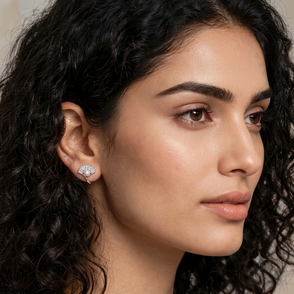 A close-up portrait of a woman with dark curly hair wearing a small silver stud earring with a fan-shaped clear gemstone setting.