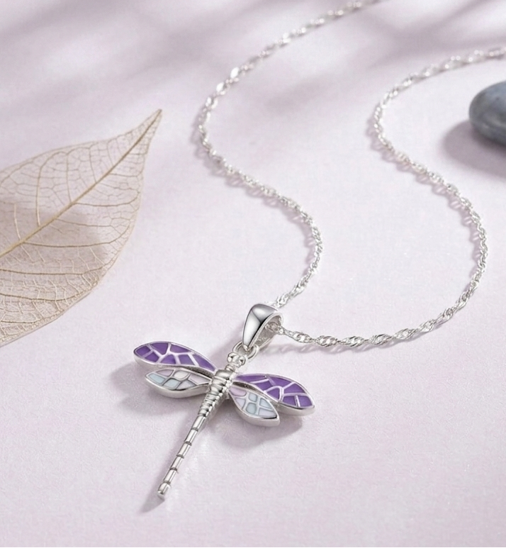 A close-up photograph of a standalone 925 sterling silver dragonfly pendant featuring intricate purple and soft blue segmented wings. The high-polish pendant features a smooth top loop, resting gracefully on a soft light lavender surface. Minimalist Indian D2C jewelry, nature-inspired charm, everyday modern styling.
