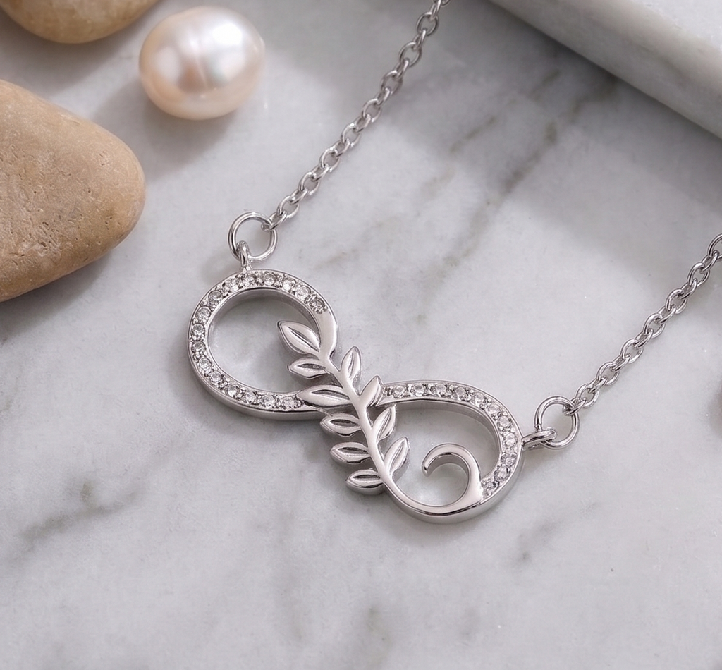 925 Sterling Silver necklace with infinity leaf design by CHAKORE on a marble surface with stones and pearls.