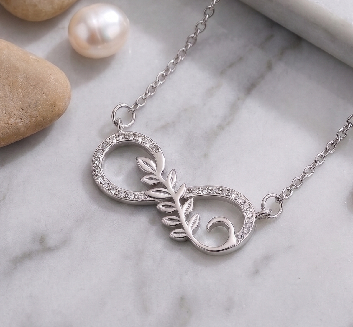 925 Sterling Silver necklace with infinity leaf design by CHAKORE on a marble surface with stones and pearls.
