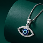 A 925 sterling silver evil eye pendant featuring a striking blue and black center surrounded by a clear crystal border. The polished pendant features a smooth top loop, displayed gracefully over a dark green background. Minimalist Indian D2C jewelry, standalone protective charm, everyday modern styling.