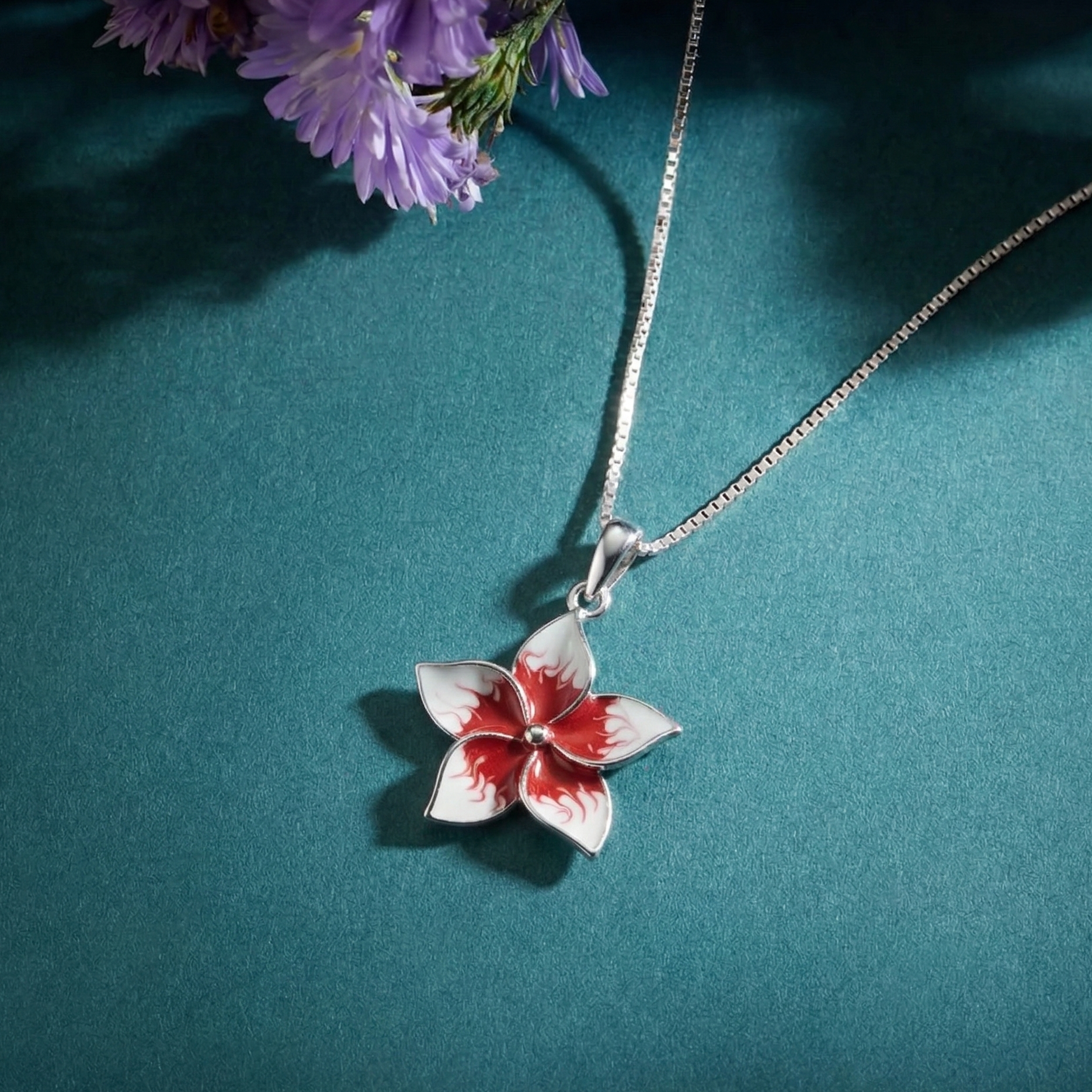 Flower-shaped pendant on a 925 silver chain against a teal background