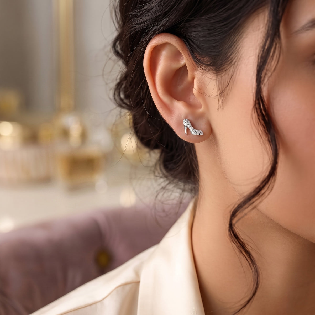 A close-up of a woman's ear wearing a small 925 silver crescent-shaped heels stud earring with sparkling clear stones, against a softly blurred indoor background by CHAKORE.