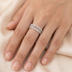 A close-up of a woman's hand resting elegantly on soft, draped peach silk fabric, modeling a wide 925 sterling silver statement ring. The ring features a repeating geometric cutout pattern bordered by delicate micro-pavé cubic zirconia stones. Modern minimalist silver jewellery, architectural wide band ring, high-polish everyday wear.