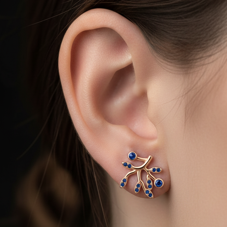 A close-up of a model's ear wearing a delicate rose gold 925 sterling silver ear cuff earring by chakore adorned with small blue stones and gold wire branches.