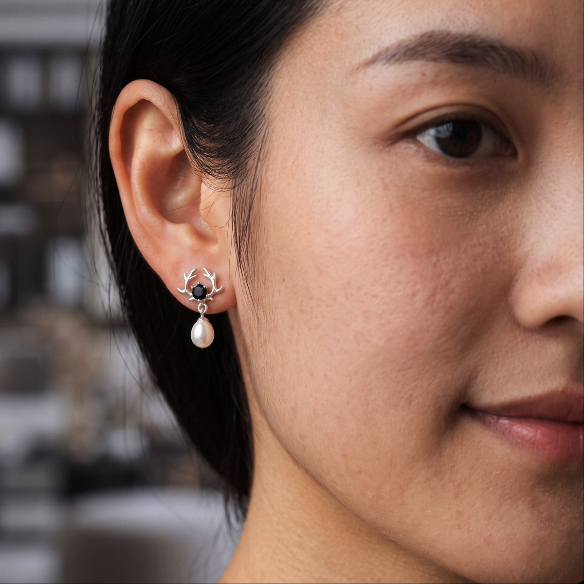 A close-up of a woman's ear wearing a small 925 silver hoop earring by Chakore with a dangling white pearl.