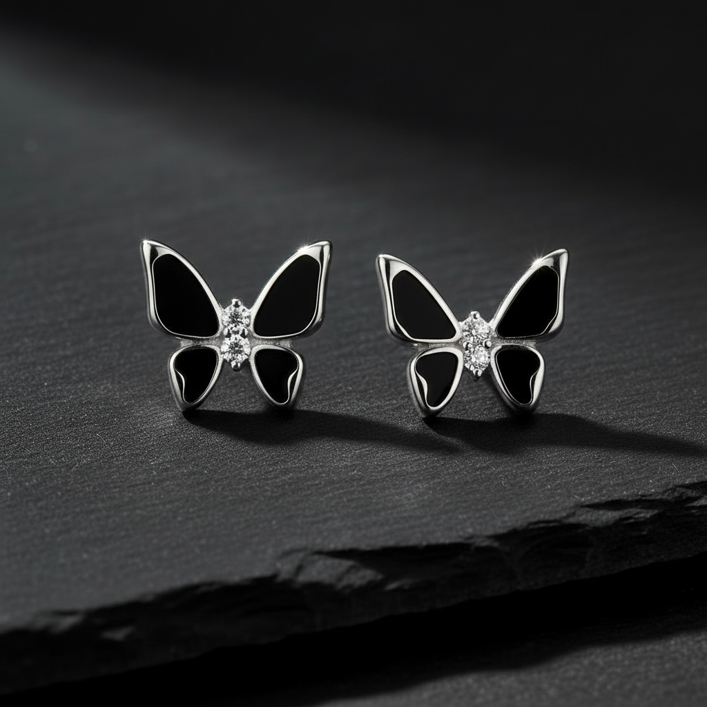 A pair of pure 925 sterling silver butterfly stud earrings with black enamel-like inlays and a small clear crystal at the center by CHAKORE, displayed on a dark textured surface.