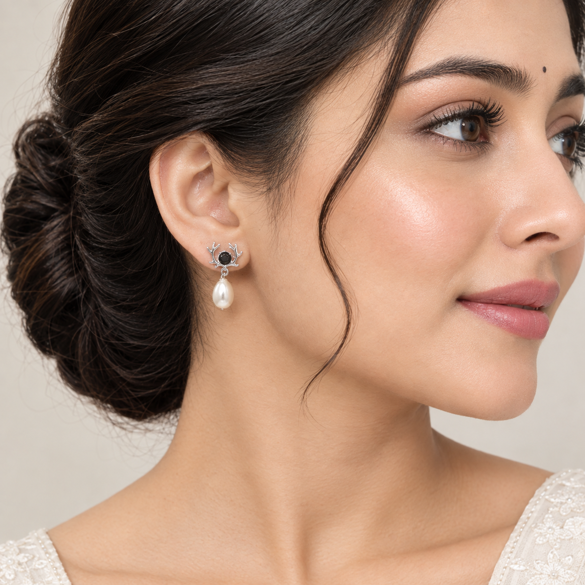 A close-up of a woman wearing a 925 silver stud earrings by Chakore with a black evil eye motif and a white pearl, shown against a soft neutral background.