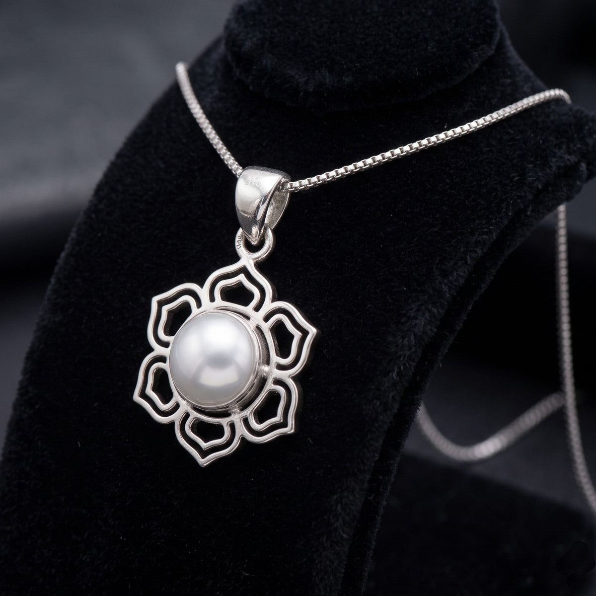 CHAKORE 925 sterling silver openwork lotus pendant with a genuine freshwater pearl, shown on a chain over black velvet.