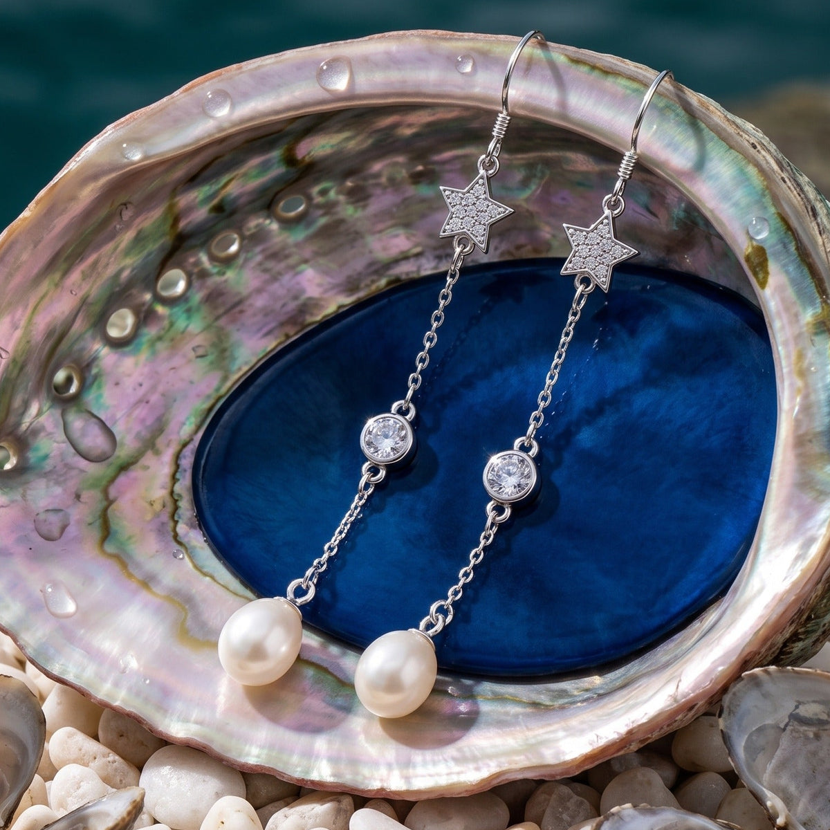CHAKORE 925 sterling silver long drop earrings with crystal stars and genuine freshwater pearls, displayed on an abalone shell.