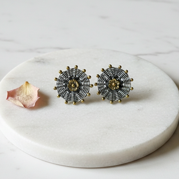 Oxidised 925 silver stud earrings with brass gold flower centre displayed on elevated white marble platform, minimal styling — CHAKORE premium silver jewellery
