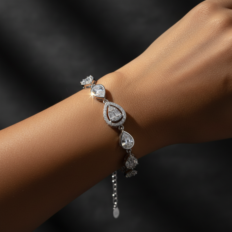 A 925 sterling silver rhodium polished bracelet by CHAKORE with teardrop-shaped clear gemstones, shown worn on a person's wrist against a dark background.