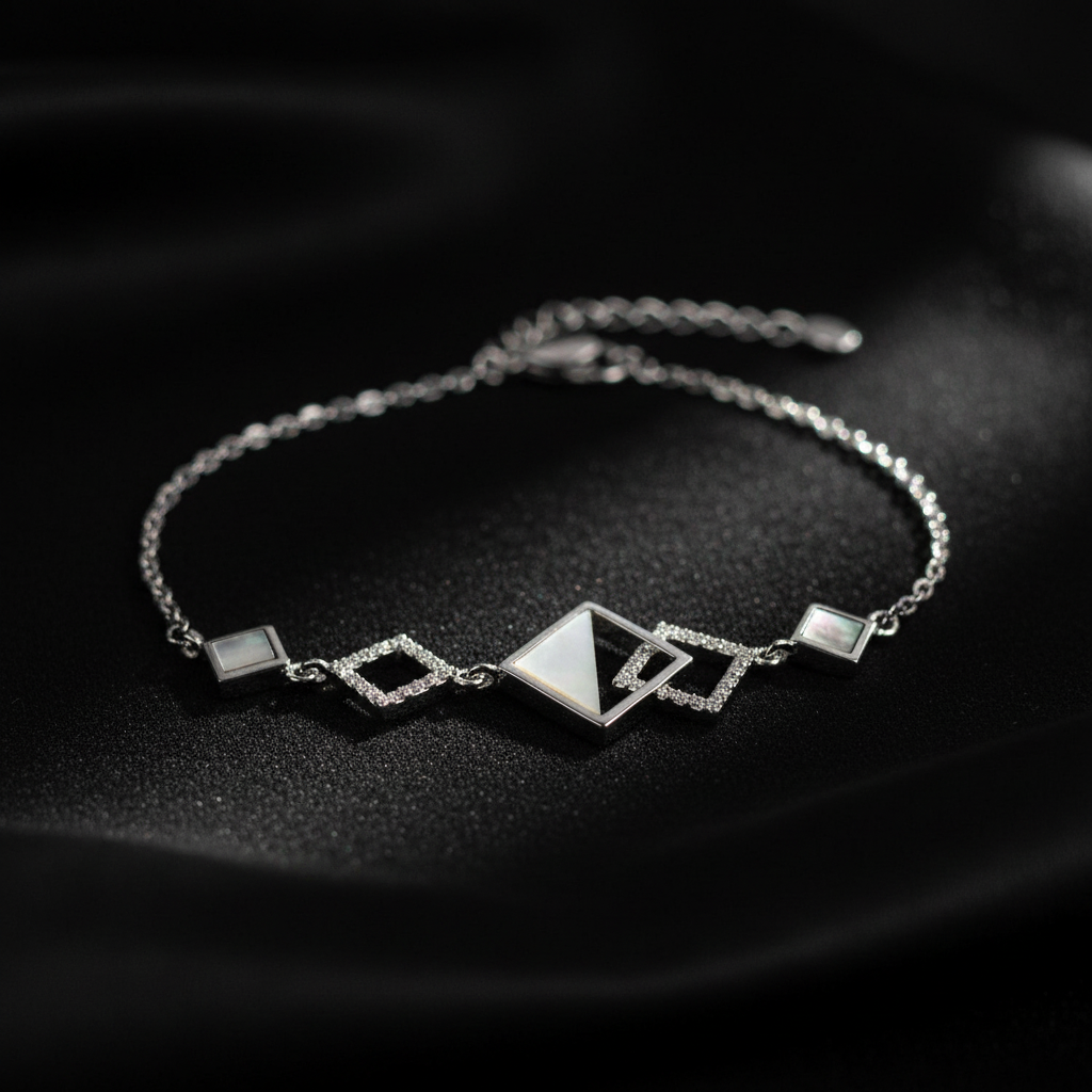 A 925 sterling silver chain bracelet by CHAKORE with geometric charms, including a central triangle and diamond shapes, accented with white inlay stones, displayed on a dark textured fabric background.