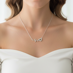 A woman with wavy brown hair wearing a delicate 925 sterling silver necklace by CHAKORE with a small heart-shaped pendant, dressed in an off-the-shoulder white top against a soft, bright white curtain background.