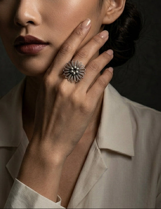 Woman wearing a oxidised 925 sterling silver flower ring by CHAKORE on her finger against a dark background