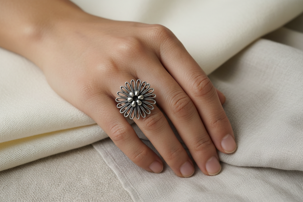 Oxidised 925 silver filigree flower ring worn on finger against soft linen and silk fabric, tactile editorial lifestyle shot
