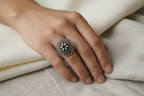 Oxidised 925 silver filigree flower ring worn on finger against soft linen and silk fabric, tactile editorial lifestyle shot
