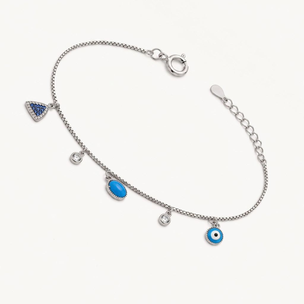A CHAKORE rhodium-plated 925 silver charm bracelet on clean whitespace. The delicate silver chain features multiple dangling motifs, including a turquoise pave triangle, an oval turquoise-colored stone, a blue and white evil eye, and bezel-set clear crystals.