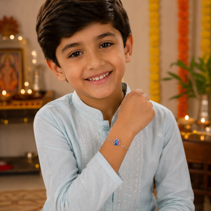 Close-up of a smiling young Indian boy wearing the Chakore Unicorn Silver Bracelet Rakhi crafted entirely in genuine 925 sterling silver, featuring a colourful enamel unicorn charm attached to a sterling silver chain with circular silver links, styled in a pastel blue festive kurta for Raksha Bandhan.